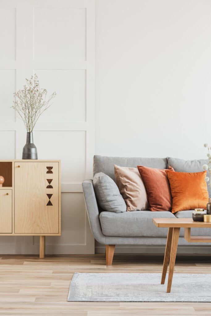 Salon moderne avec canapé gris, coussins terracotta et beige, buffet en bois clair avec motifs géométriques et fleurs séchées dans un vase gris.